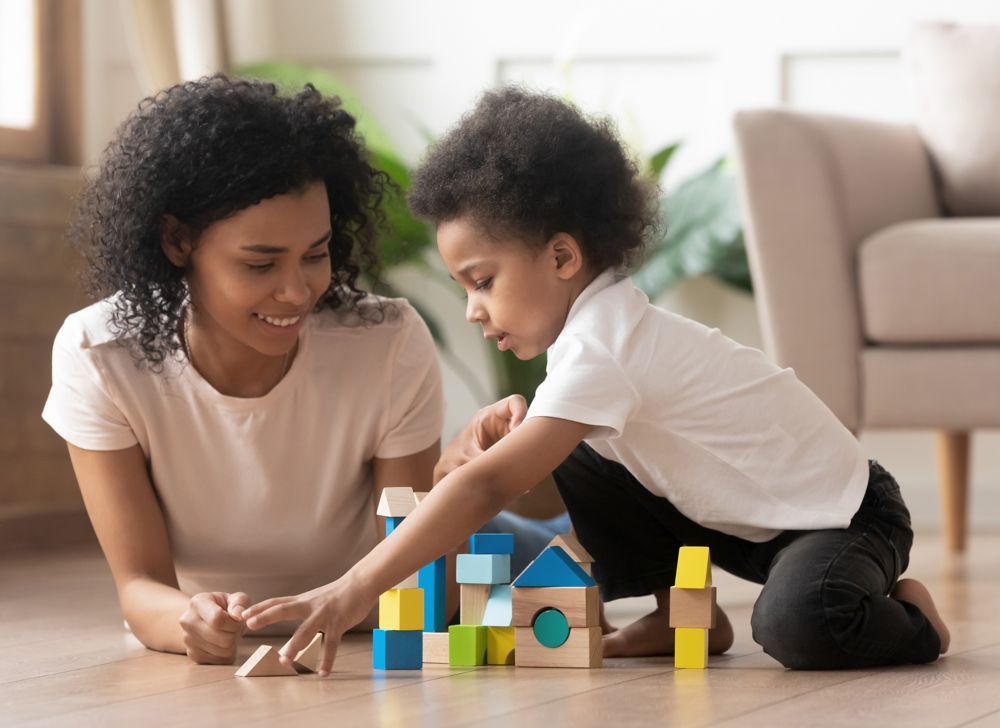 A mother and child play with blocks on a wood floor. 
