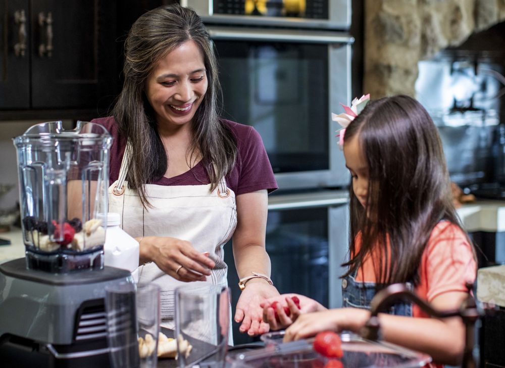 A mother and daughter prepare berries to make smoothies in a blender. 