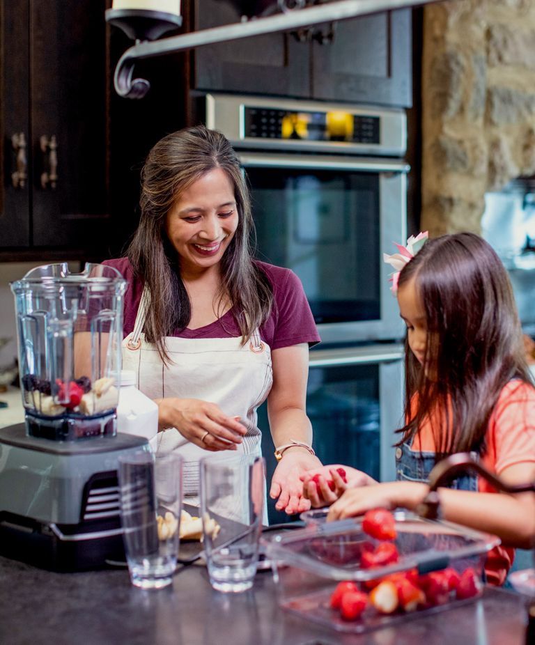 A mother and daughter prepare strawberries to make smoothies in a blender. 