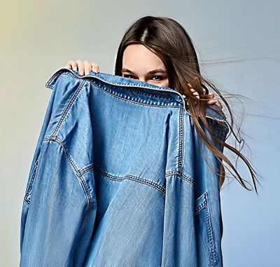 A person holds a denim jacket up to their face.  