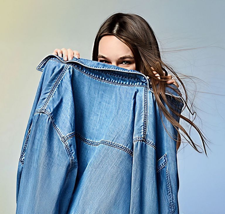 A person holds a denim jacket up to their face.  