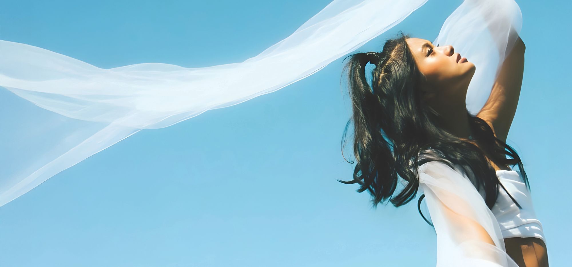 Woman raising their arms as a white fabric flows in the wind. 