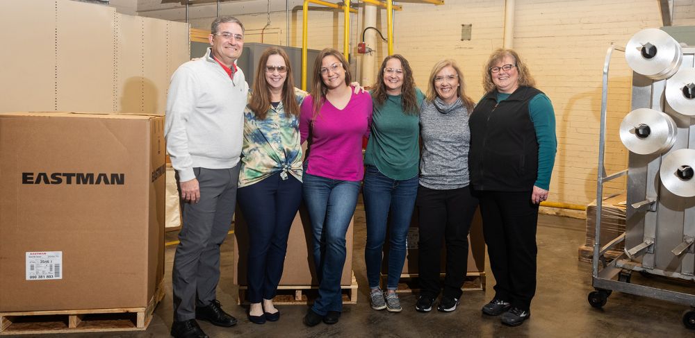 Six textiles team members pose with Eastman shipping boxes. 