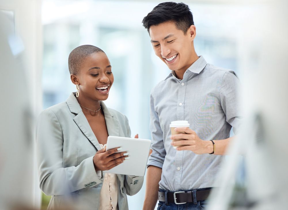Two office employees smiling and discussing notes. 