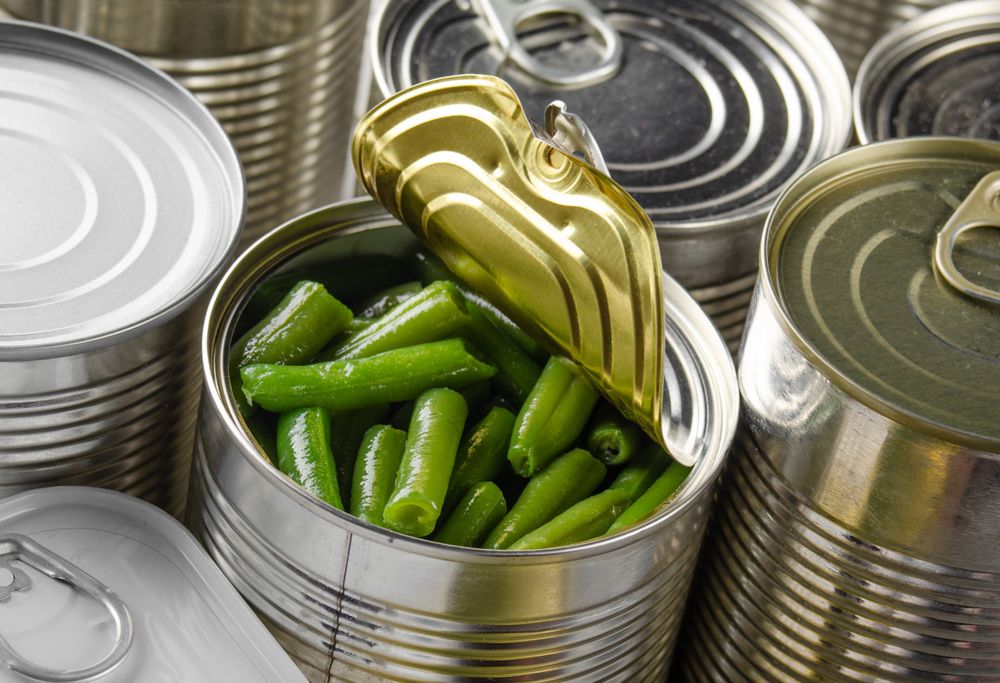Amid a series of closed cans sits one open can of green beans. 