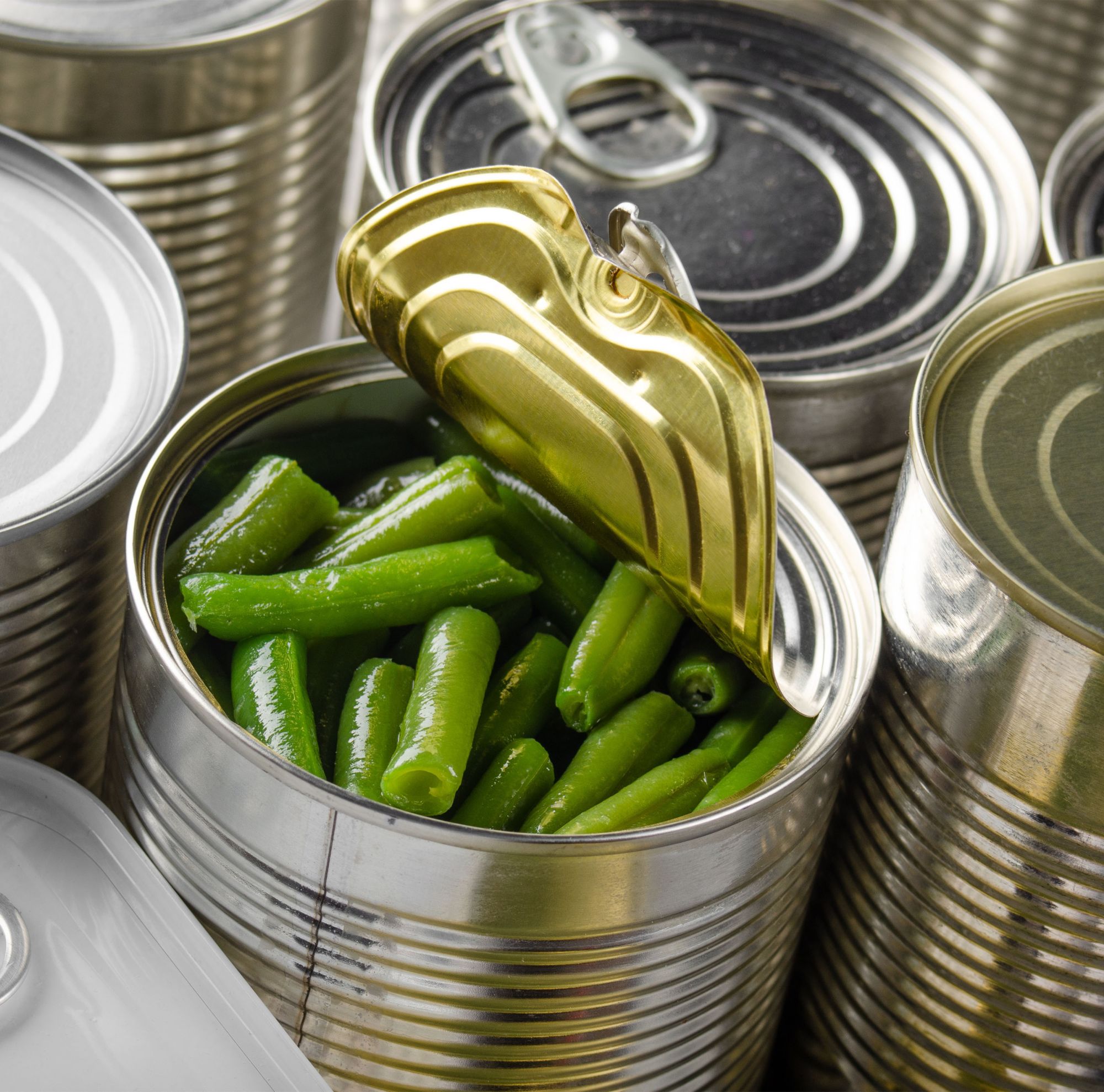 An open can of green beans sits with several other closed cans. 
