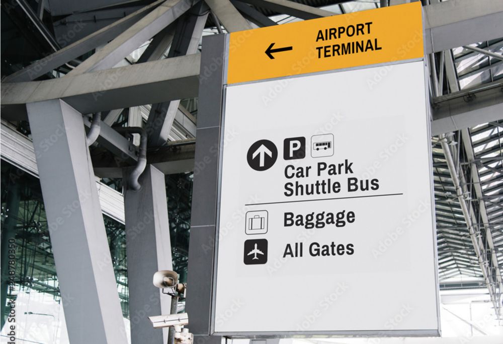 A sign inside an airport directs visitors to the terminal, parking area, baggage claim and gates. 
