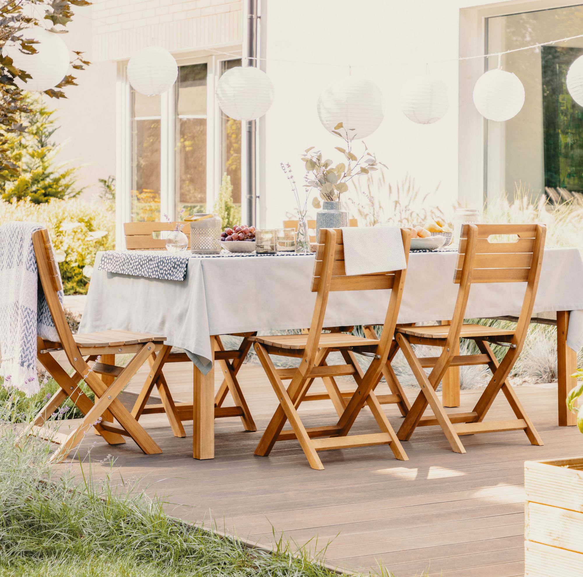 Wooden folding chairs surround a patio table covered by a white tablecloth. 