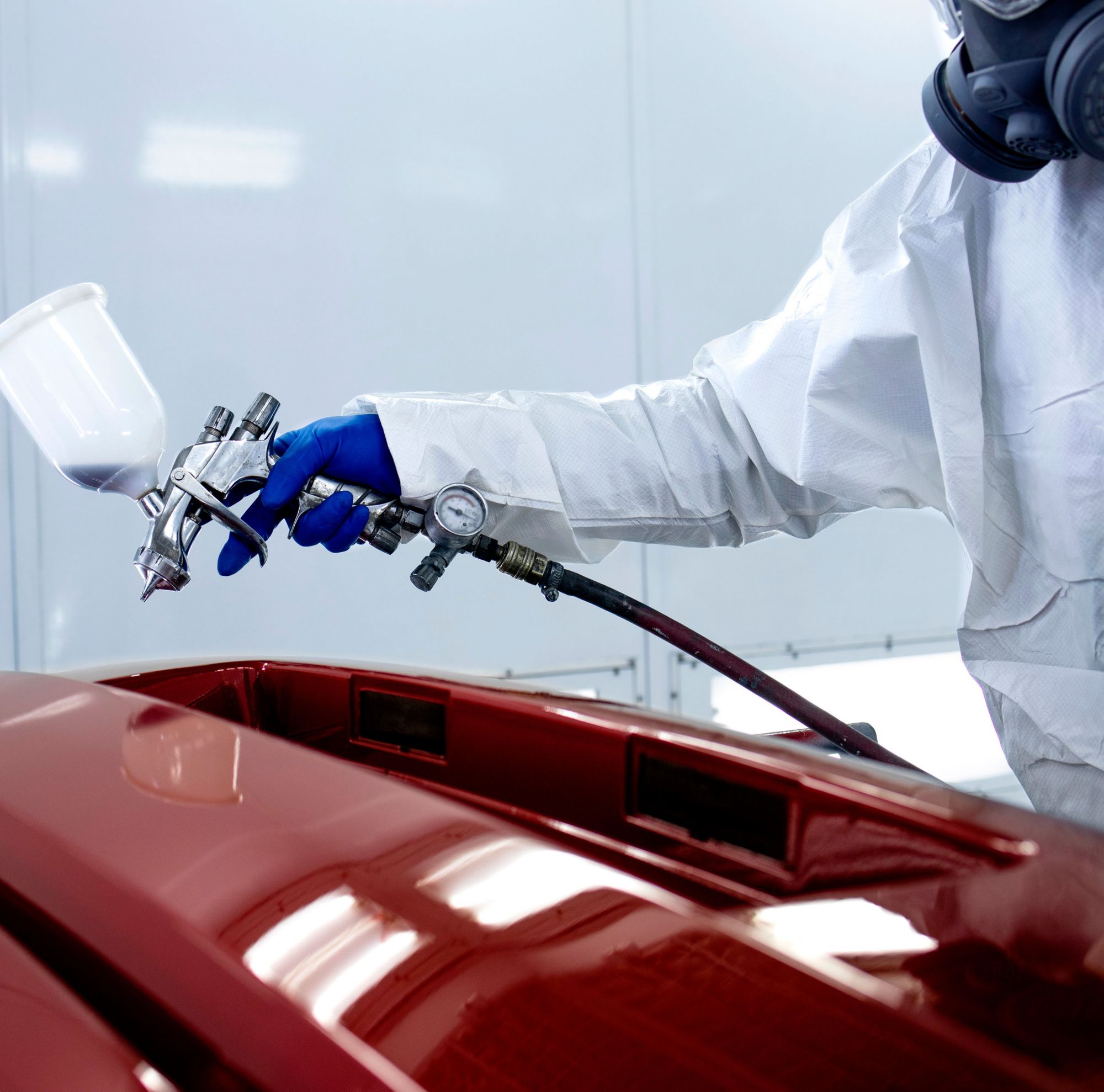 A painter spray paints a car red in a shop. 
