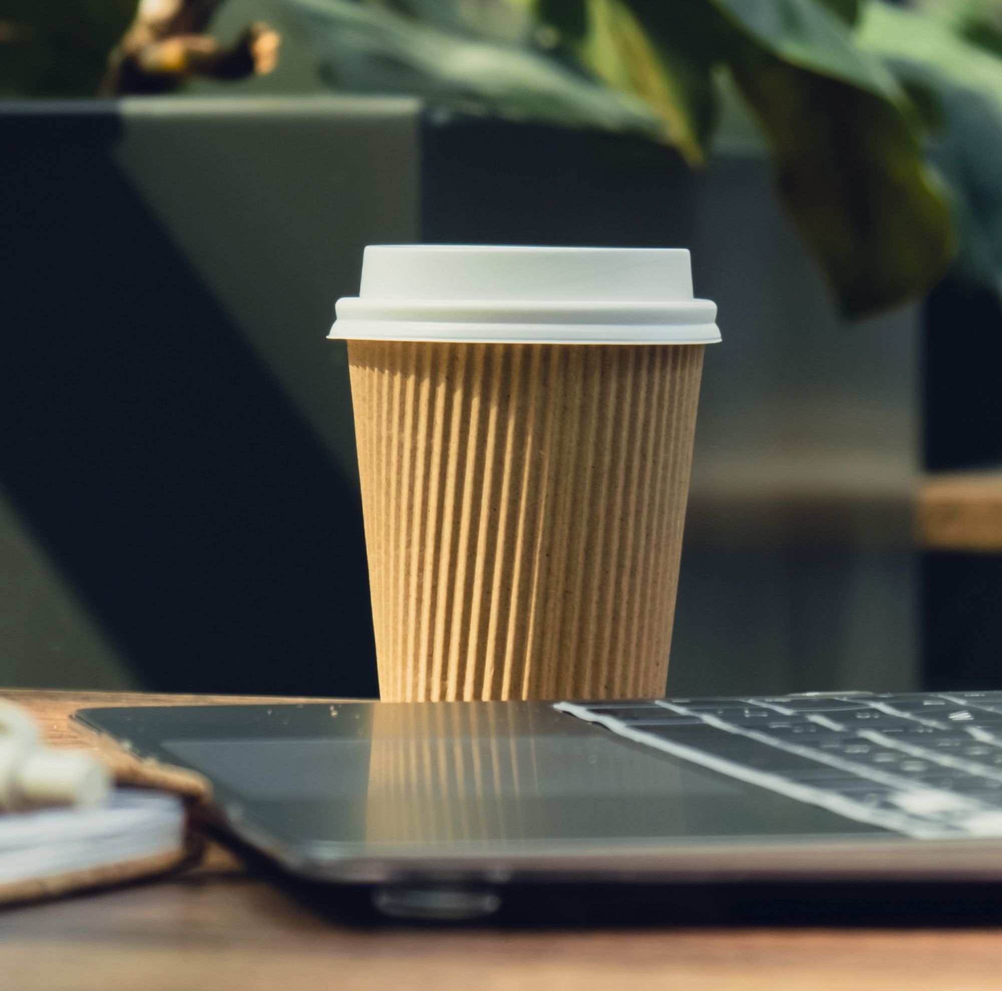 A paper coffee cup sits next to a laptop on a table. 