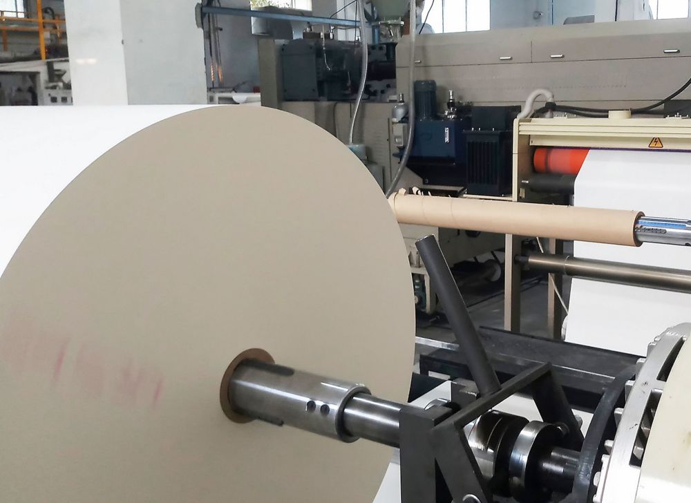  A large roll of coated white paper is being fed through a machine. 