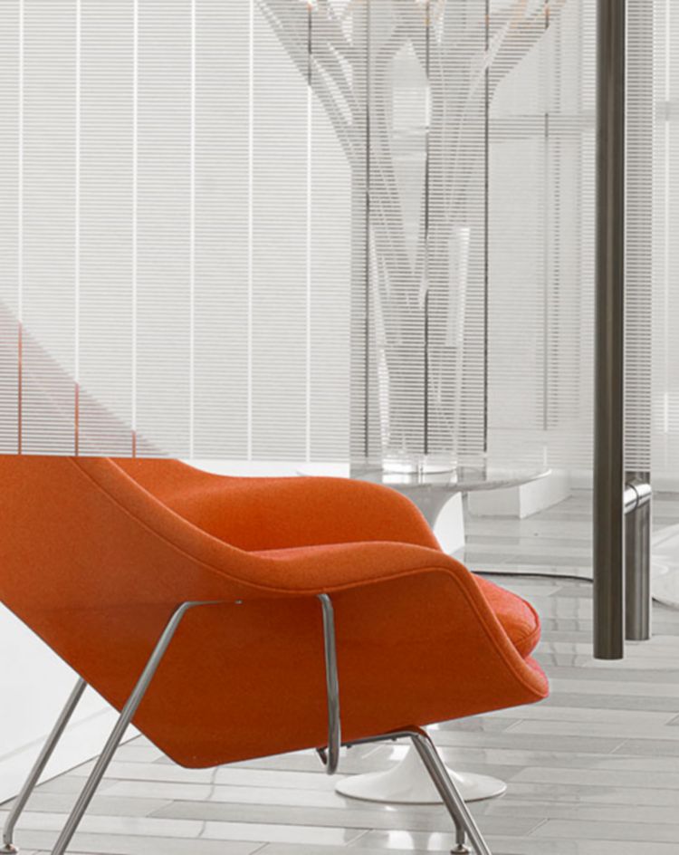 Modern office lounge with orange upholstered chairs and small white tables, viewed through glass walls with subtle horizontal privacy lines. 
