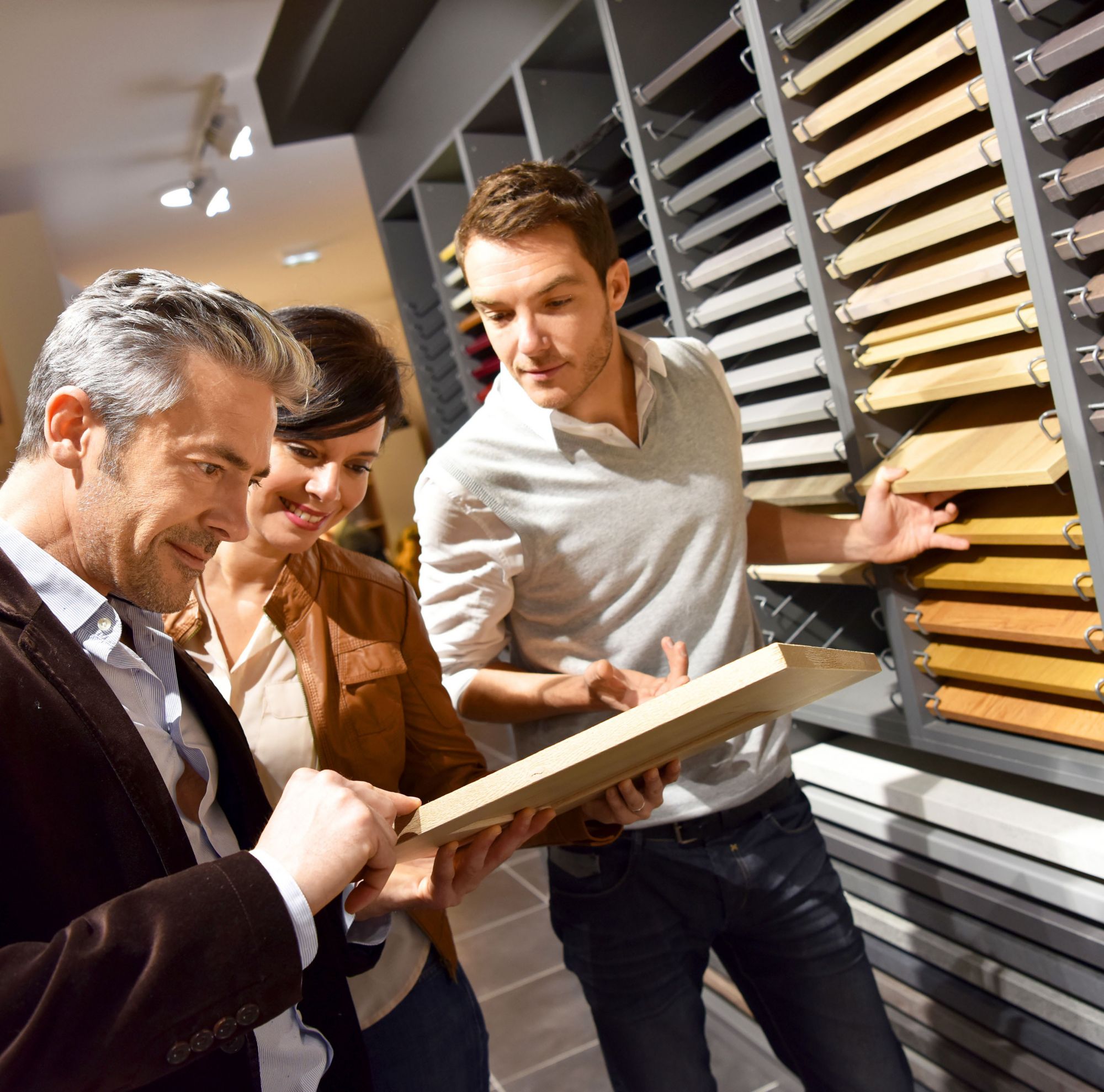 Three people review differently colored wood samples that sit on shelves. 