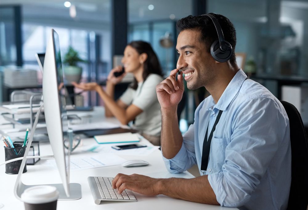 Two customer service agents take phone calls in front of computers in an office. 