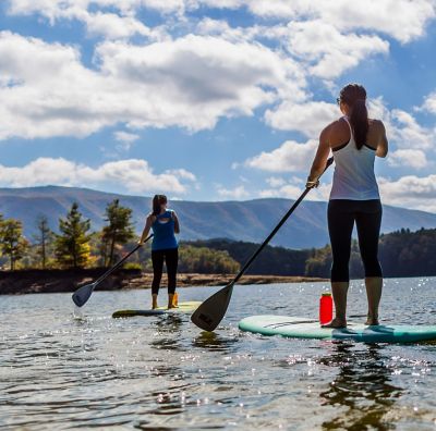 Two women on standup paddle boards at a lake.