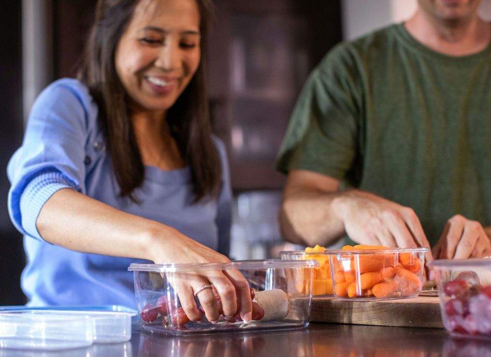 A woman reaches into a reusable food storage container. 
