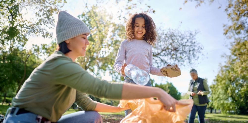 Two people recycling a water bottle and brown paper bag at a park. 