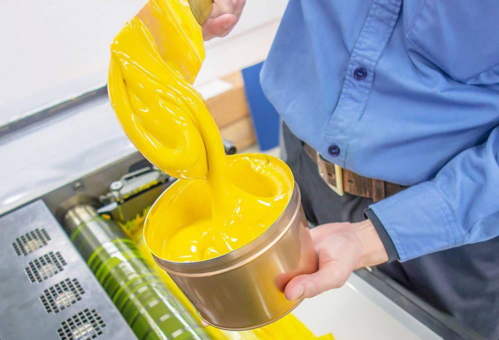 A person adds yellow from a container onto a printing press. 