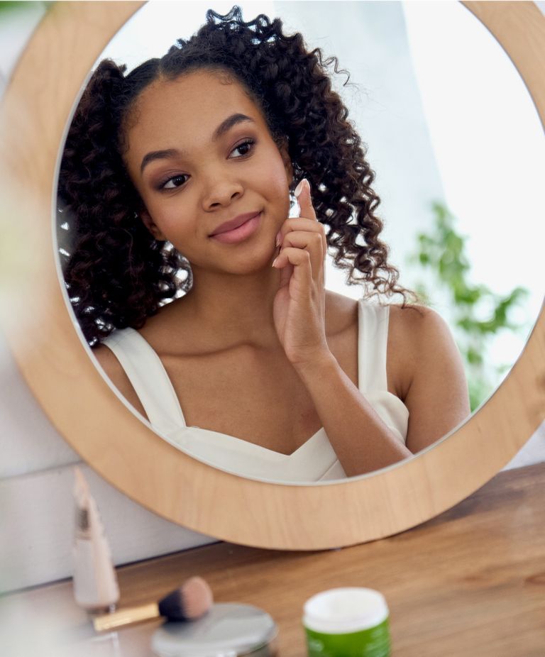 A woman looks at her reflection in a mirror and applies cream.  