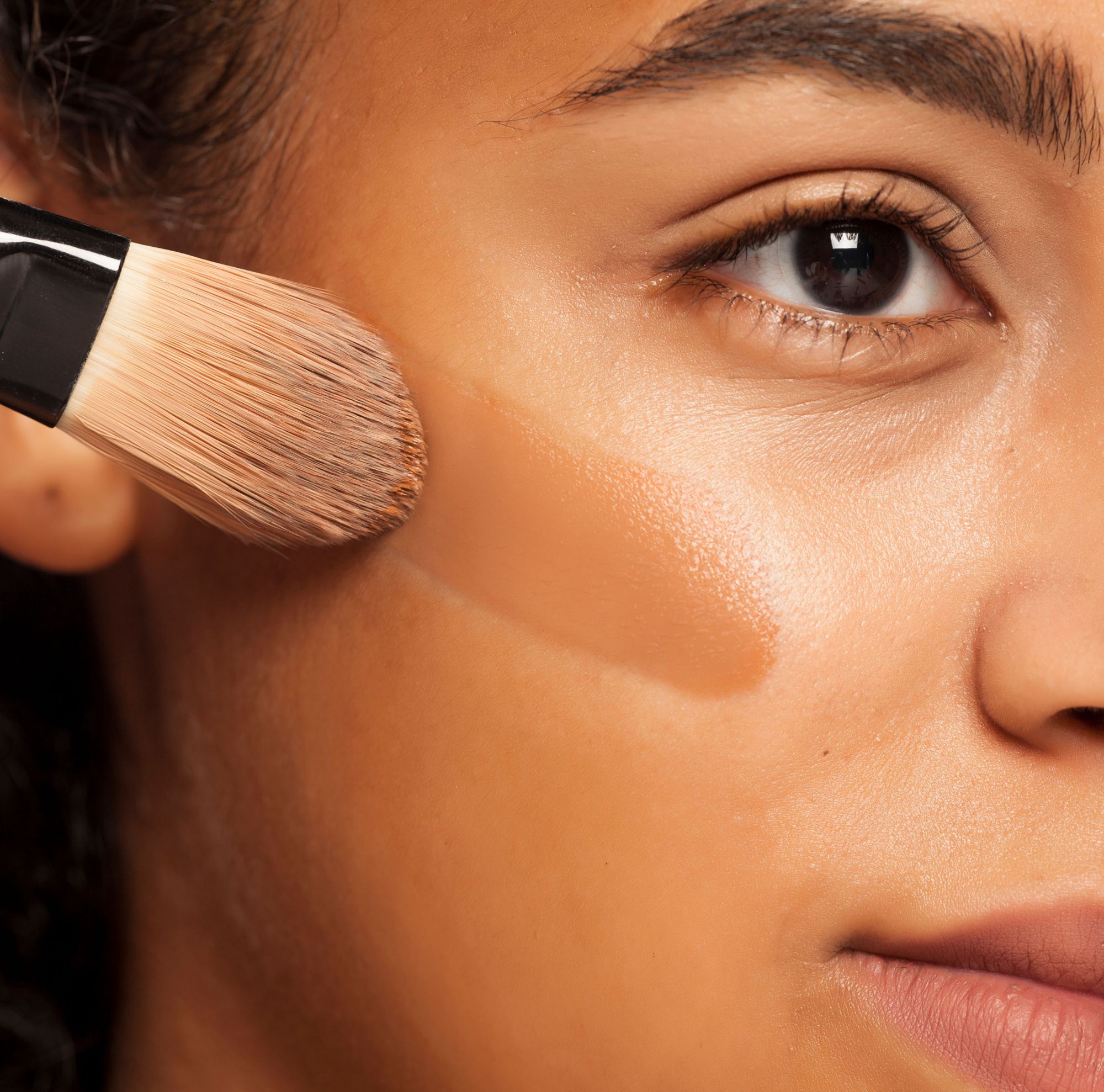 A person applies liquid foundation to their cheek with a brush. 