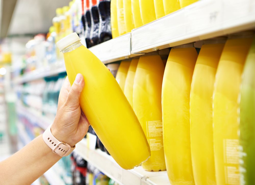 A yellow beverage bottle is picked up from a store shelf. 