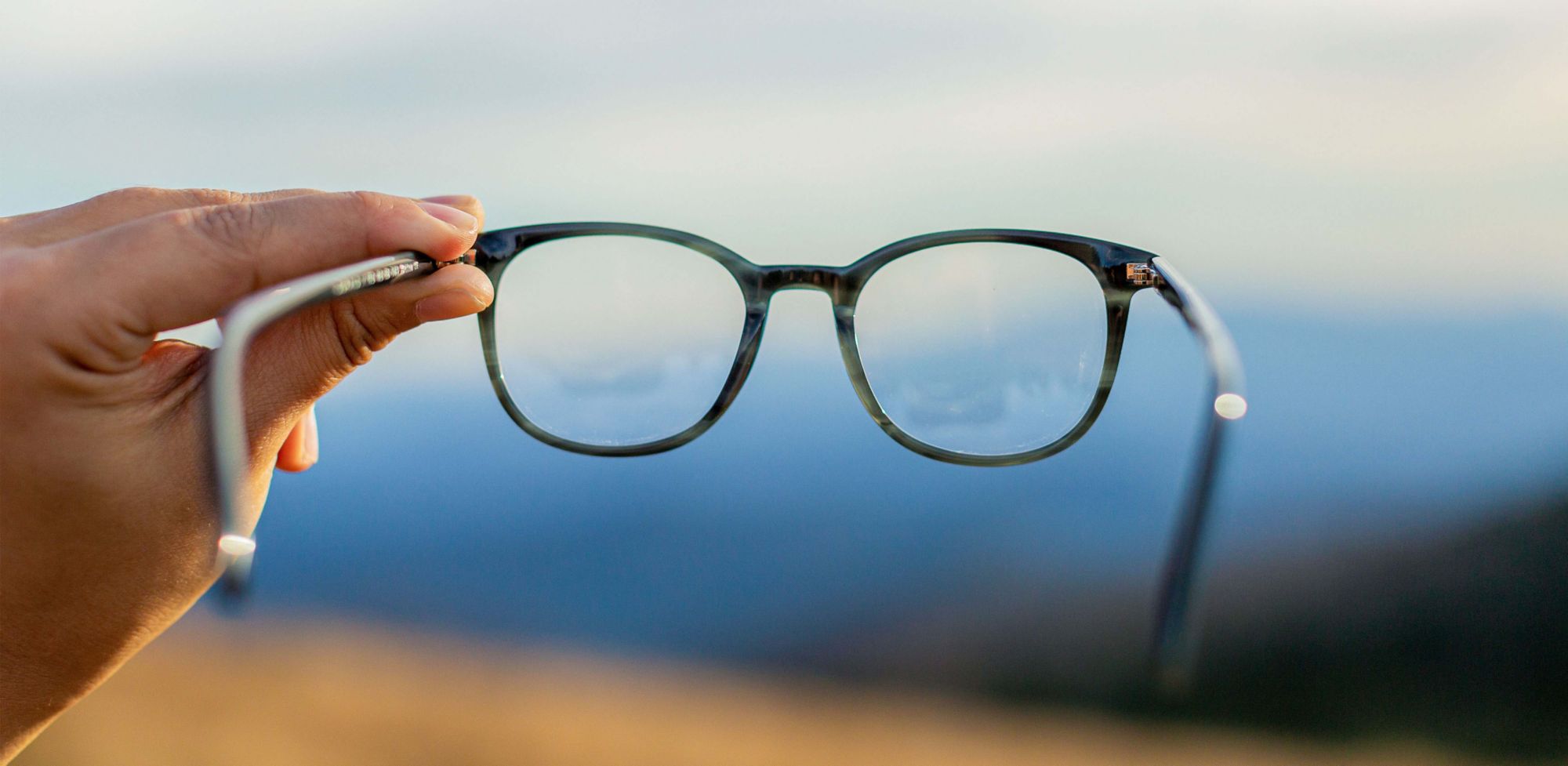 A person holding glasses in front of a view of mountains. 
