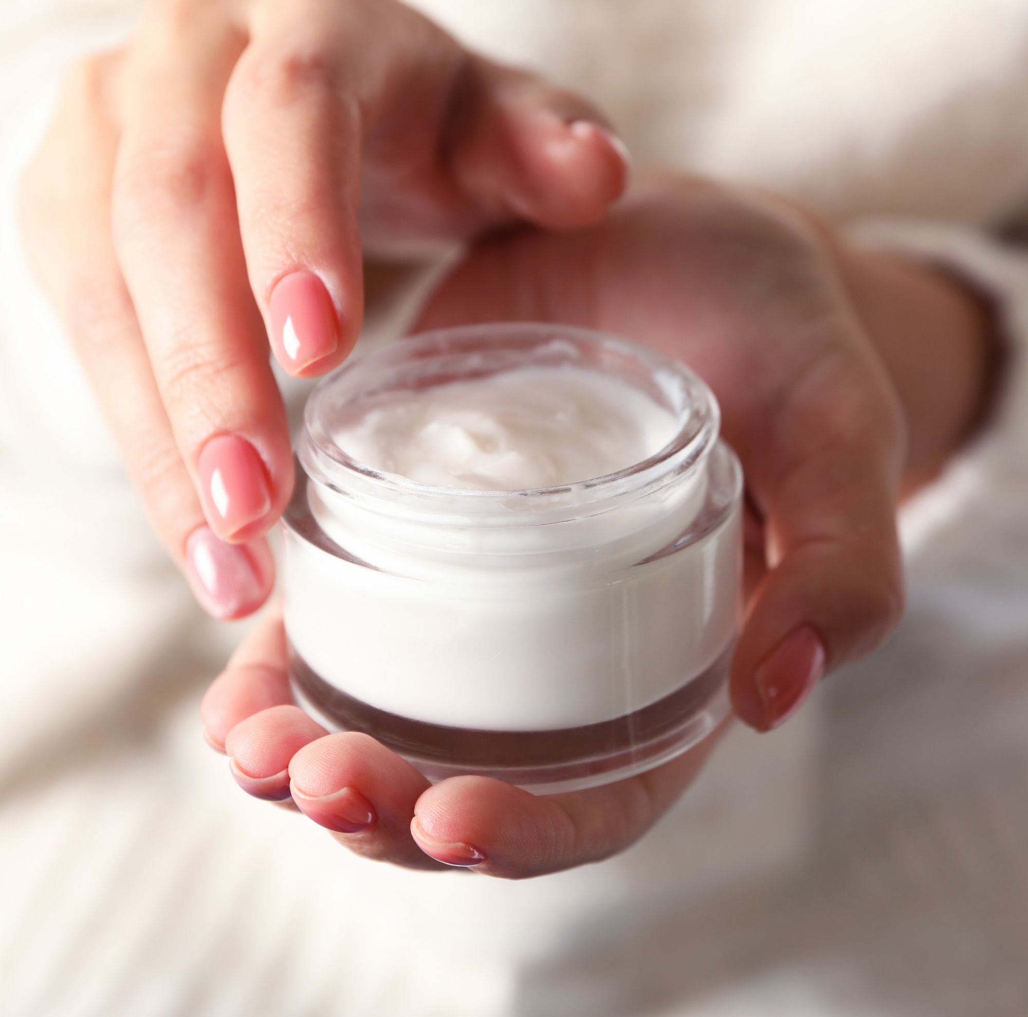 Close-up of hands holding a clear jar of skin care cream 