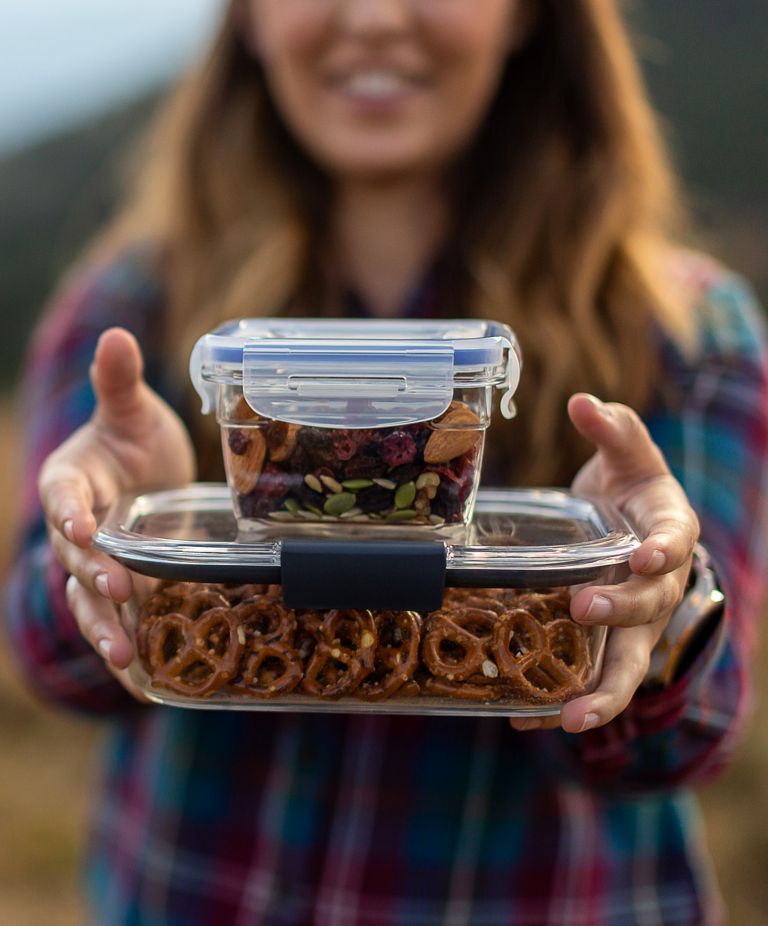 A woman holds two Tritan food storage containers with snacks inside.  
