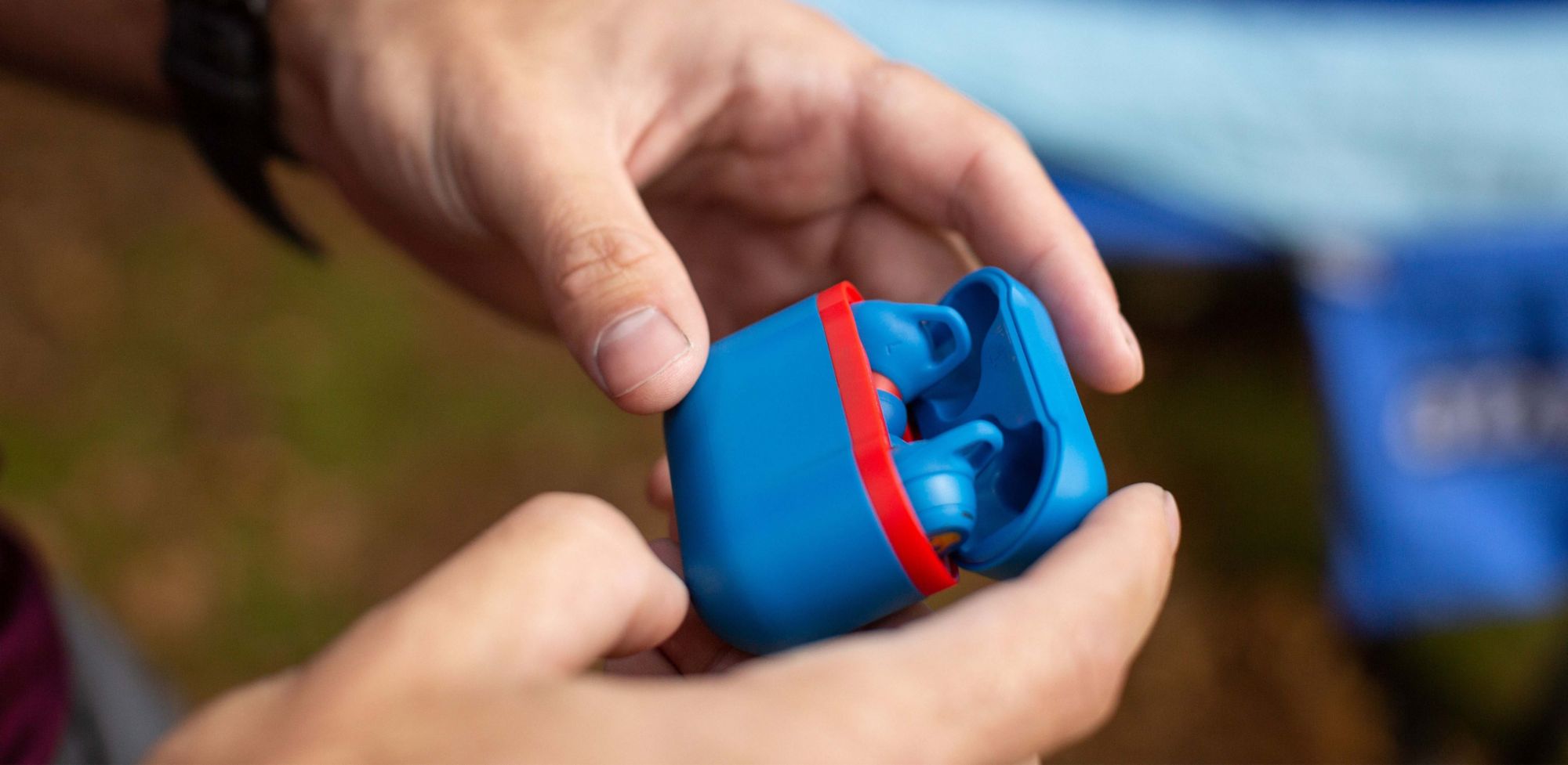 A person holds a blue and red case with earbuds. 