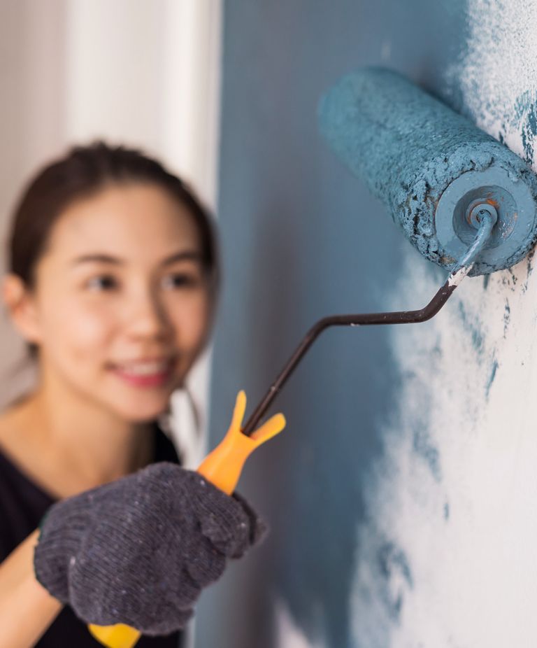 A woman rolls grayish blue paint onto a wall. 
