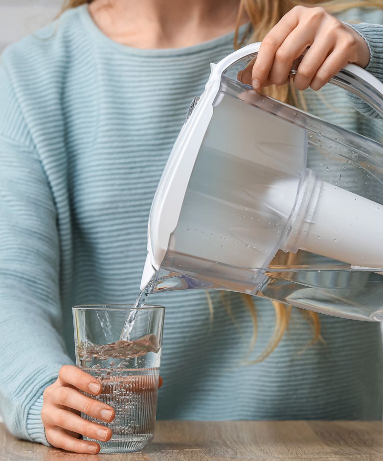 A person pouring water from a water filtration pitcher into a clear cup. 