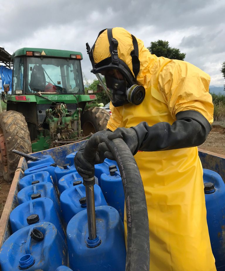 A person wearing a yellow hazmat suit, complete with a full-face respirator mask and black gloves, filling up jugs with Nemasol 