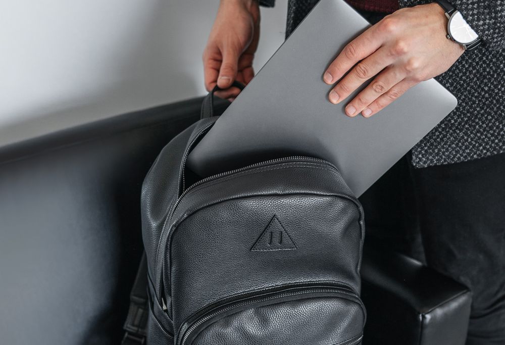 A person loading a laptop into a black leather backpack. 
