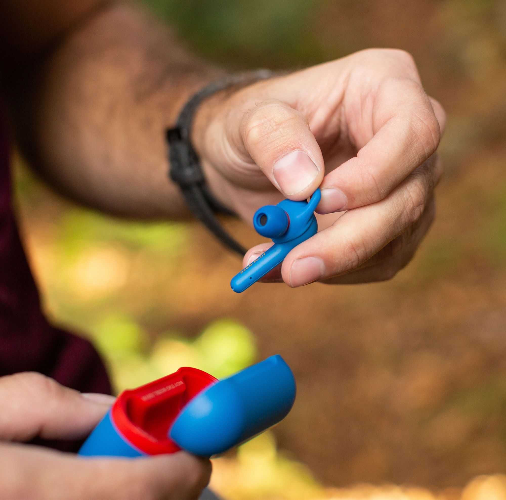A person removes a blue earbud from its case. 