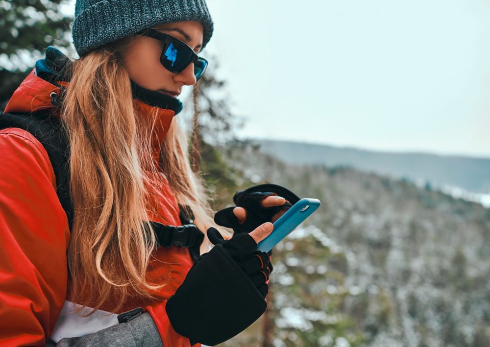 Person in snow gear using phone in the mountains. 