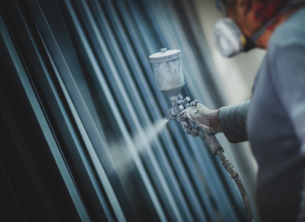 A masked man applies blue spray paint to a metal wall. 