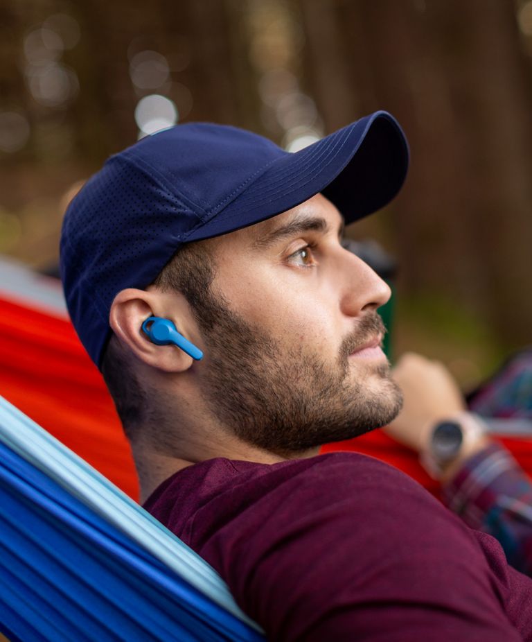 A man rests in a hammock with blue cordless earphones. 