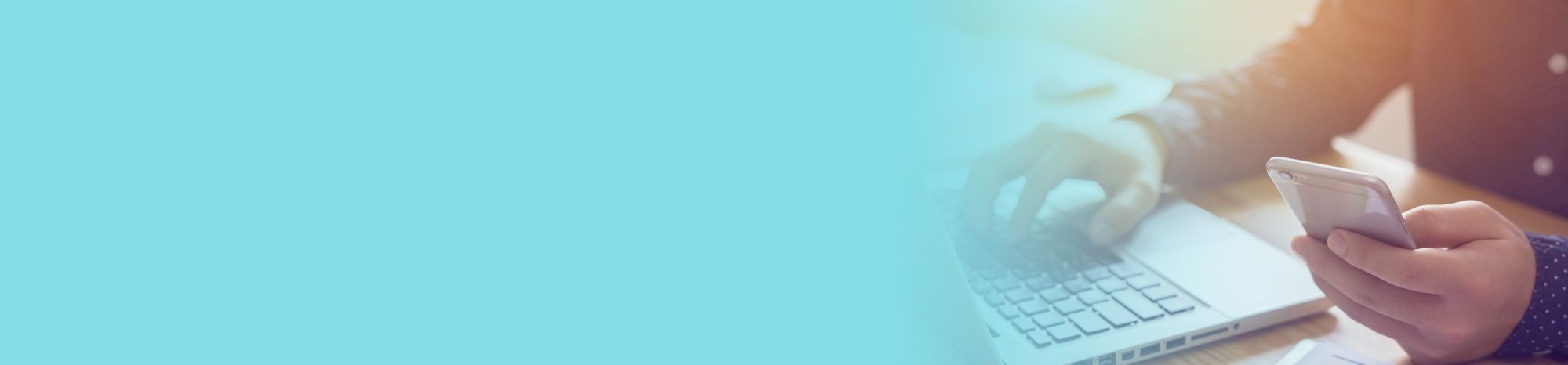 One hand is typing on a laptop keyboard, and the other is holding a cellphone. 