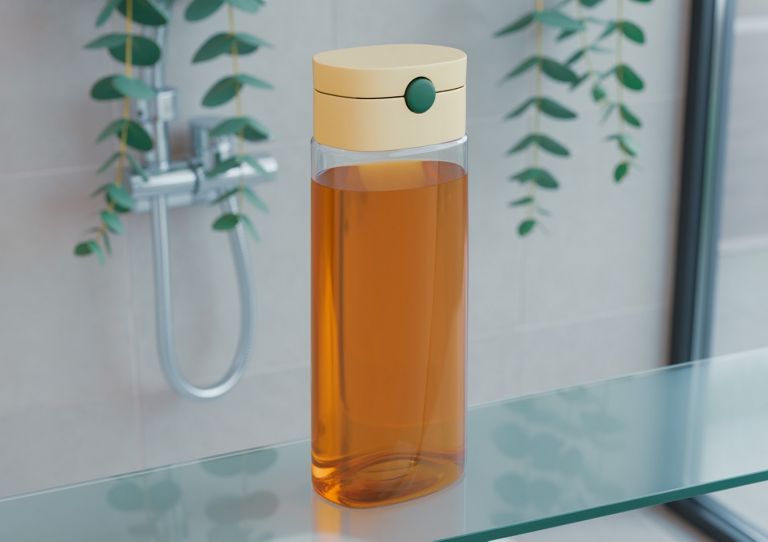 A clear plastic bottle filled with orange shampoo on a bathroom countertop. 