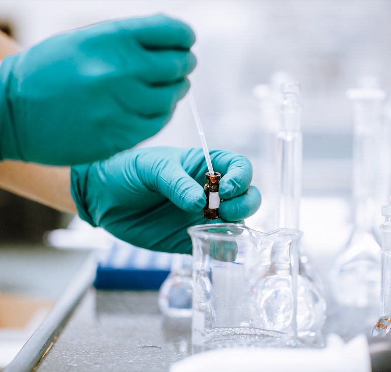 A researcher pipettes a clear liquid from a small vial. 