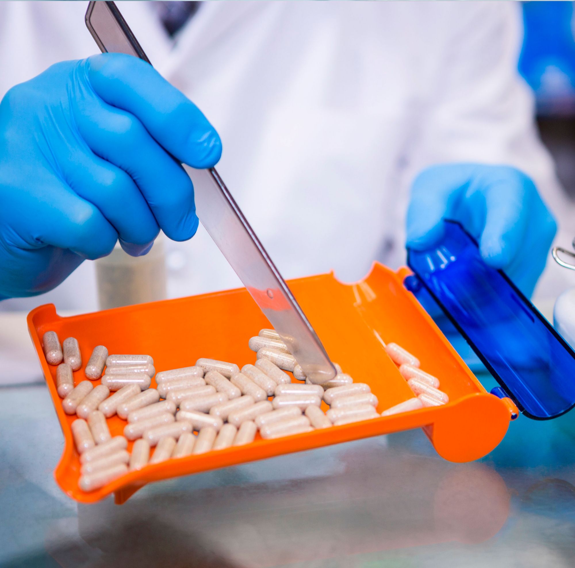 A pharmacist uses a pill counting tray and metal spatula to count pills. 
