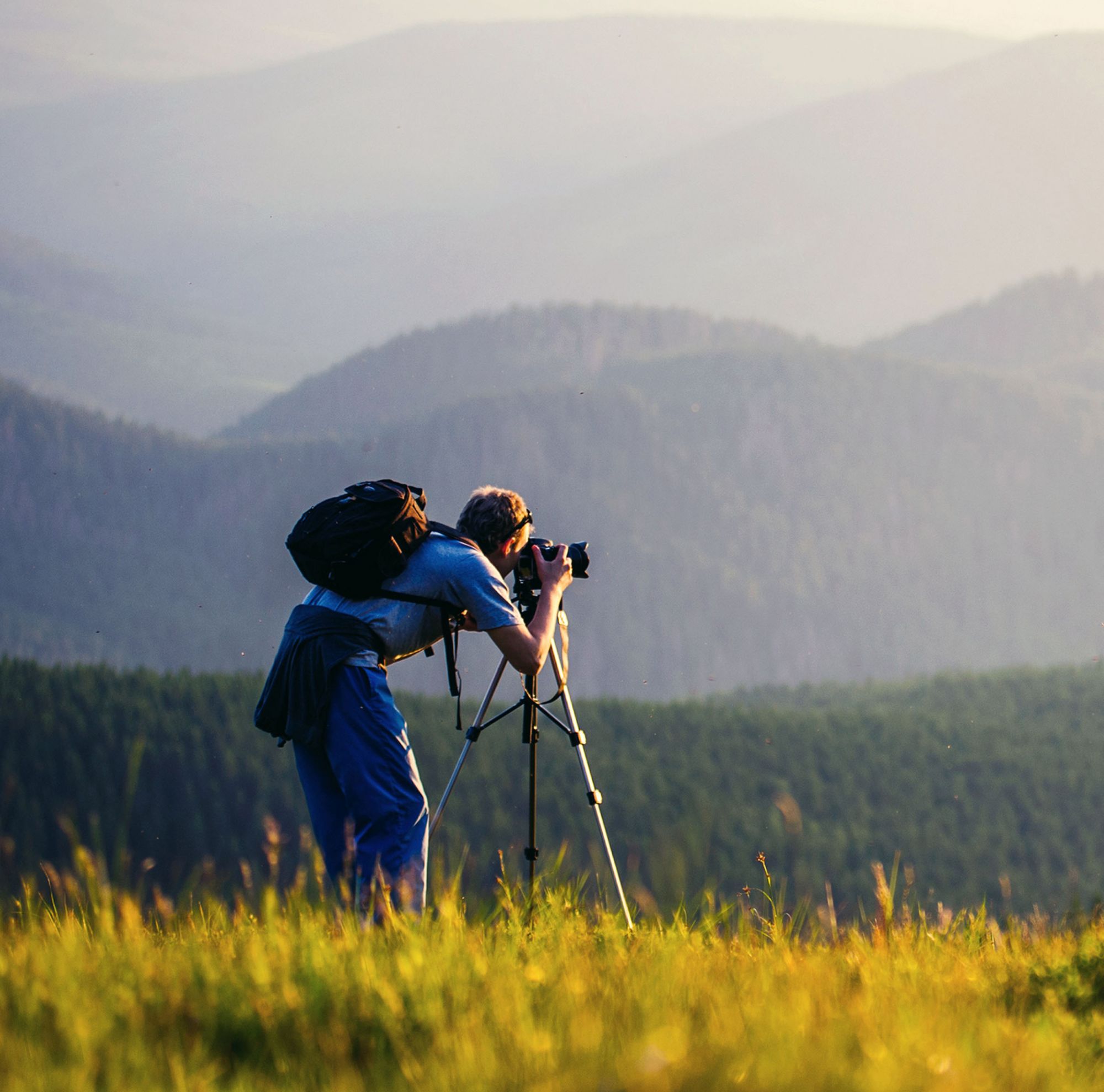 A man with a camera on a tripod takes a picture of the surrounding mountains. 