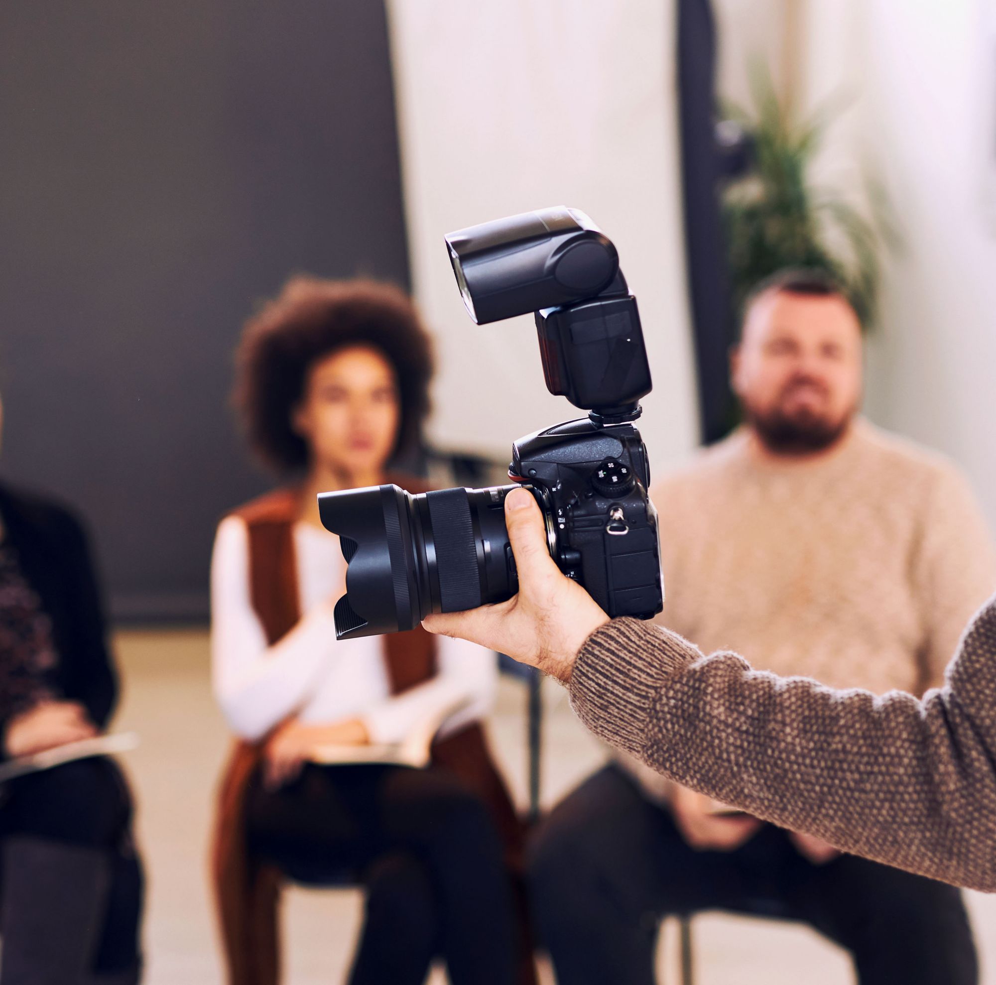 A woman looks into a camera viewfinder as three people watch her. 