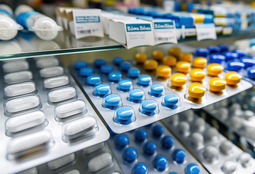 An assortment of pills in medicine blister packs on a pharmacy shelf. 
