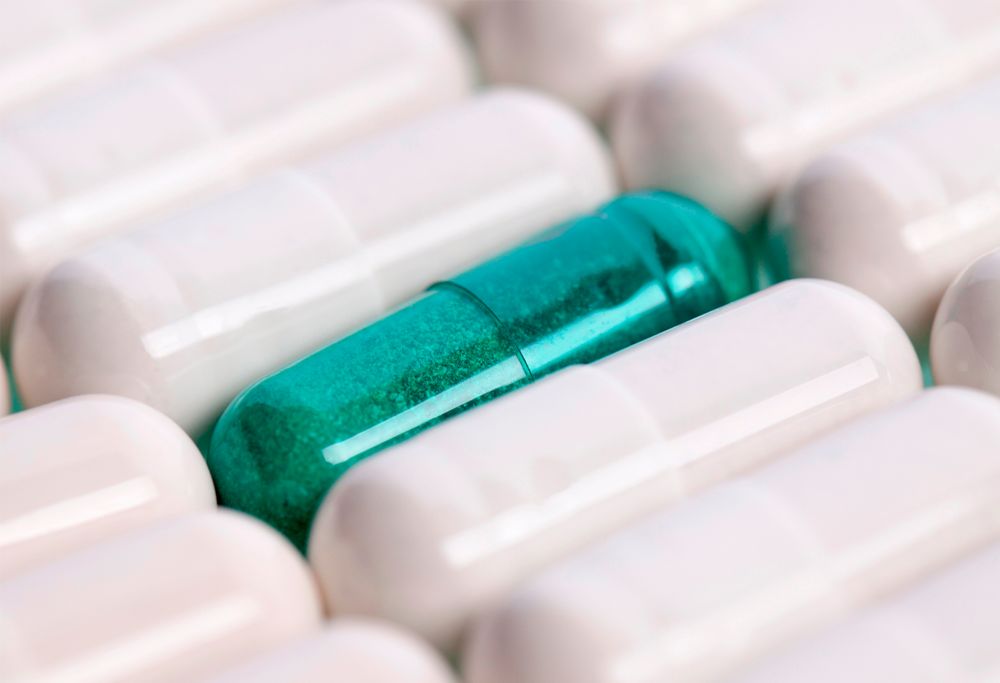 A green pill among a group of white pills.  