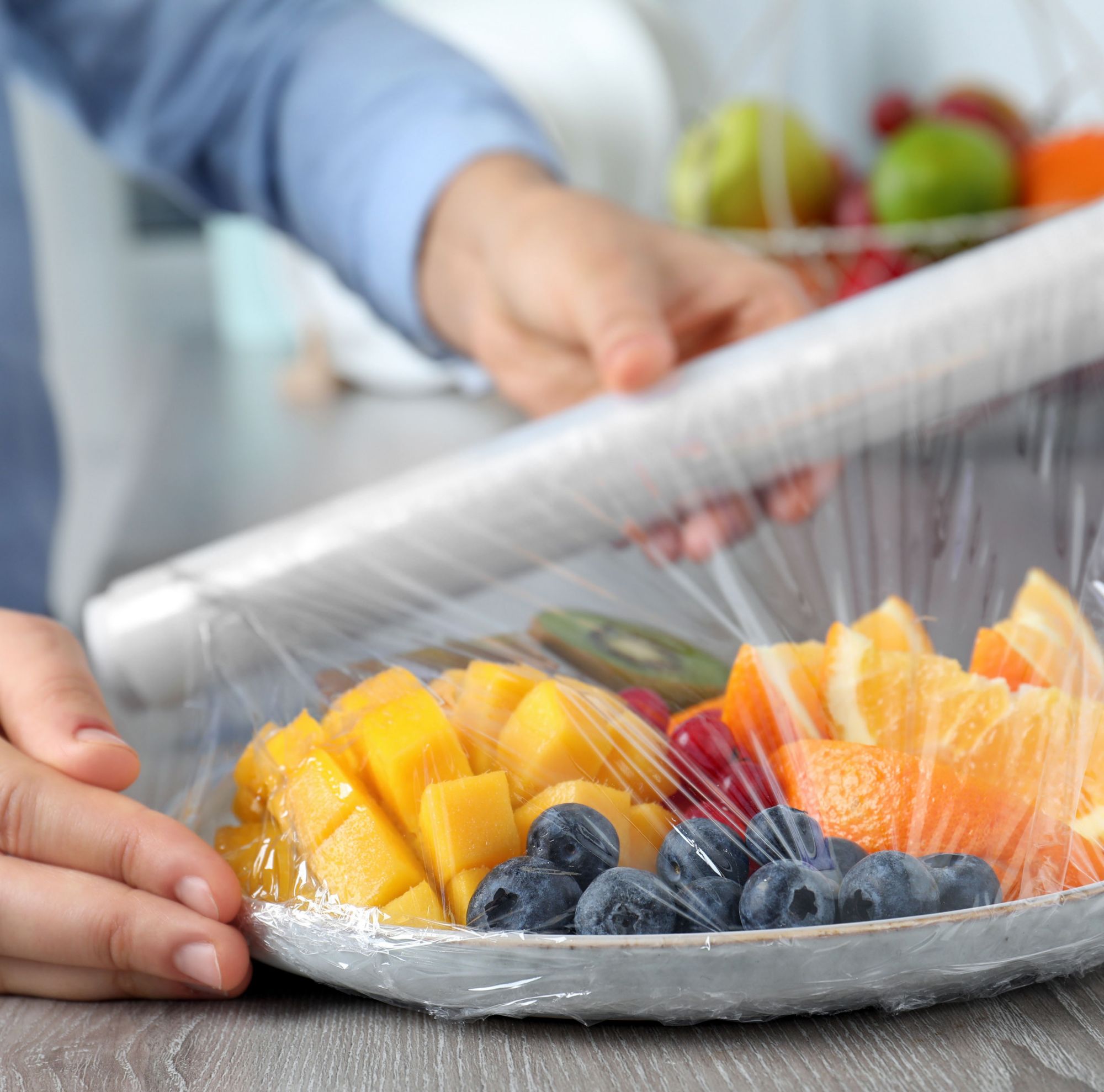 A person puts plastic wrap over a plate of fruit. 