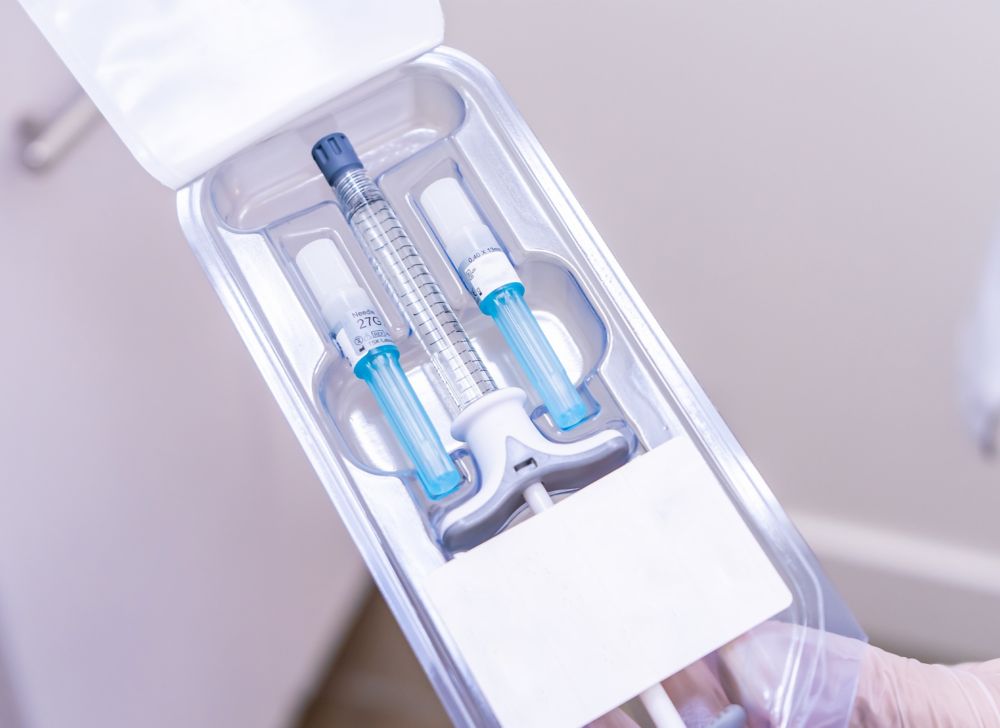 Clear medical packaging containing a syringe, with two concealed needles positioned on either side.  
