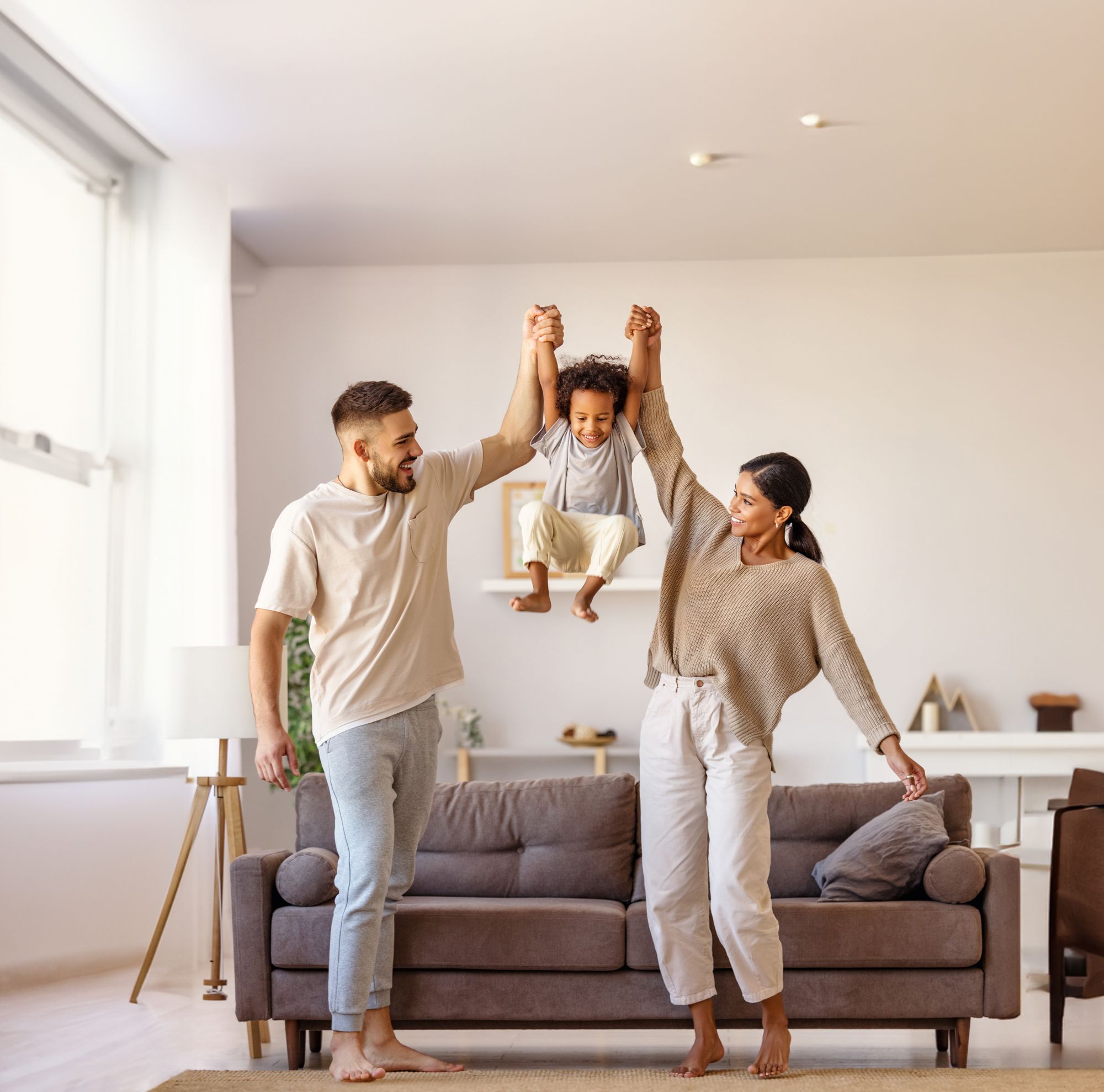 Two parents swing their laughing child between their arms. 