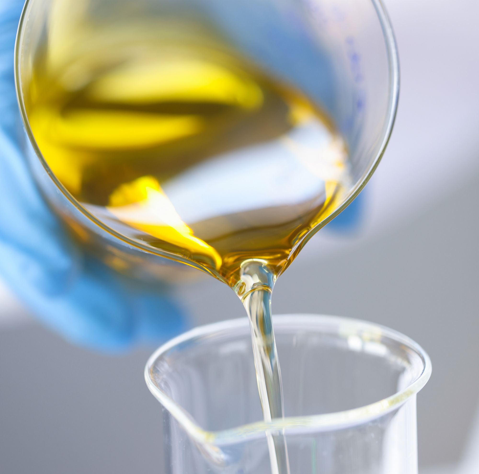 A scientist pours yellow liquid into a smaller beaker. 