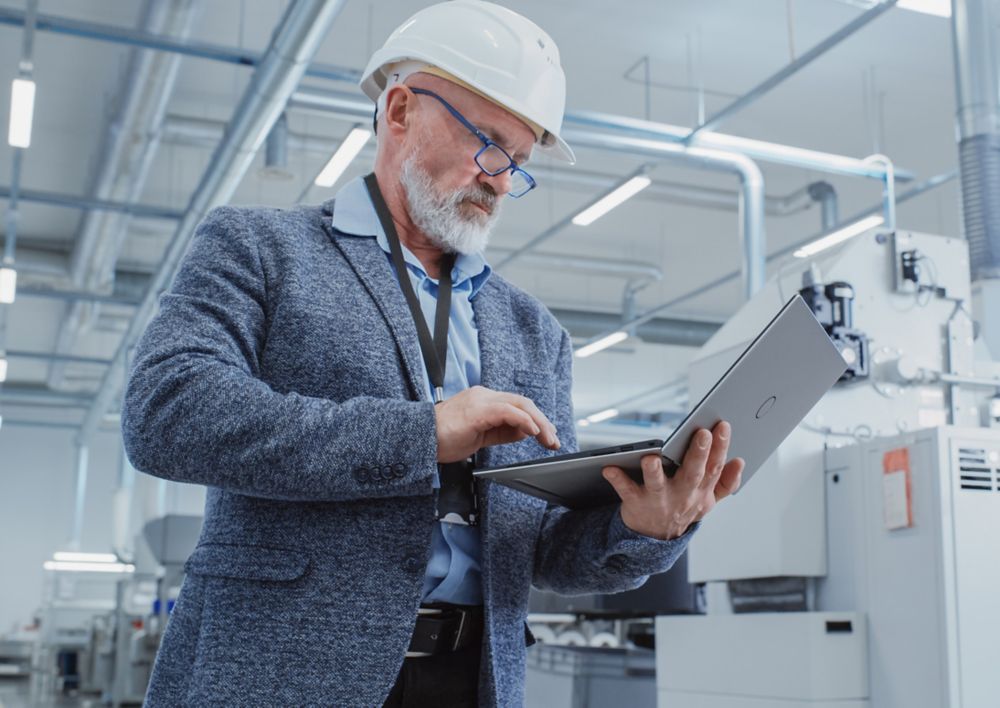 An engineer wearing a hard hat and using a laptop in the lab. 